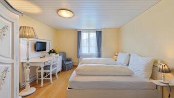 Habitación de hotel con cama, escritorio con silla, televisor y ventana con cortinas.