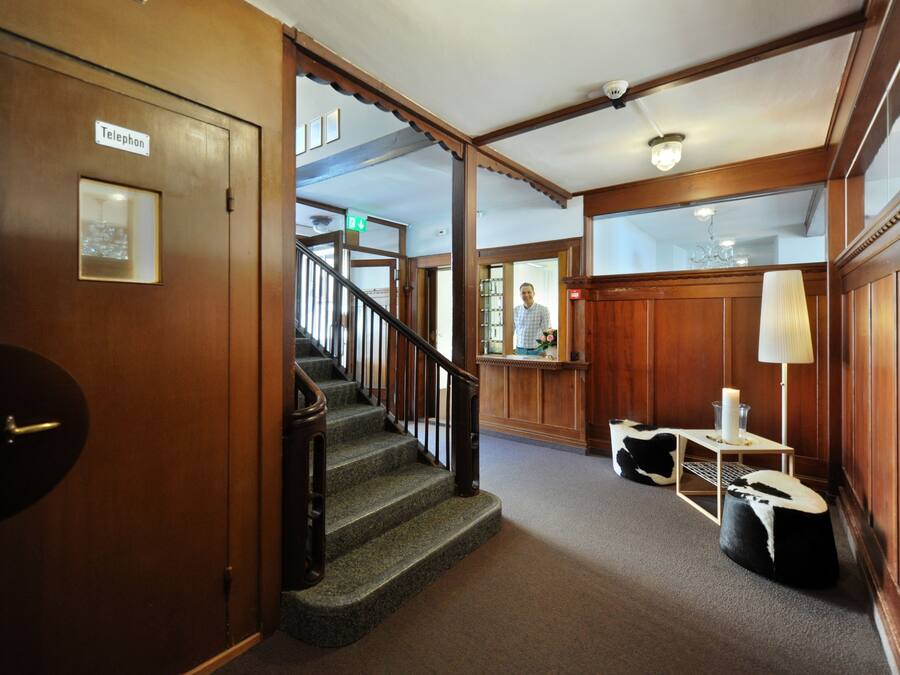 A wooden interior with a staircase, a reception desk, and a telephone sign.