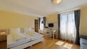 Una habitación de hotel con cama, escritorio, televisor y ventana con cortinas.