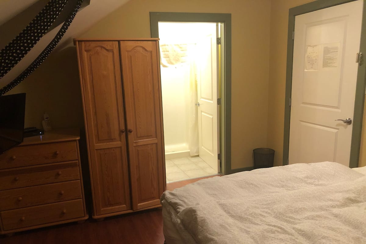 Une chambre à coucher comprenant un lit, une armoire, un bureau avec un téléphone et une porte donnant sur une salle de bain.