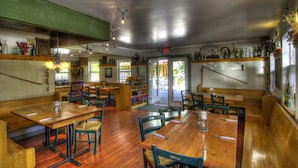 Een restaurant met houten tafels en stoelen, een groene prikbordwand en diverse flessen op planken.