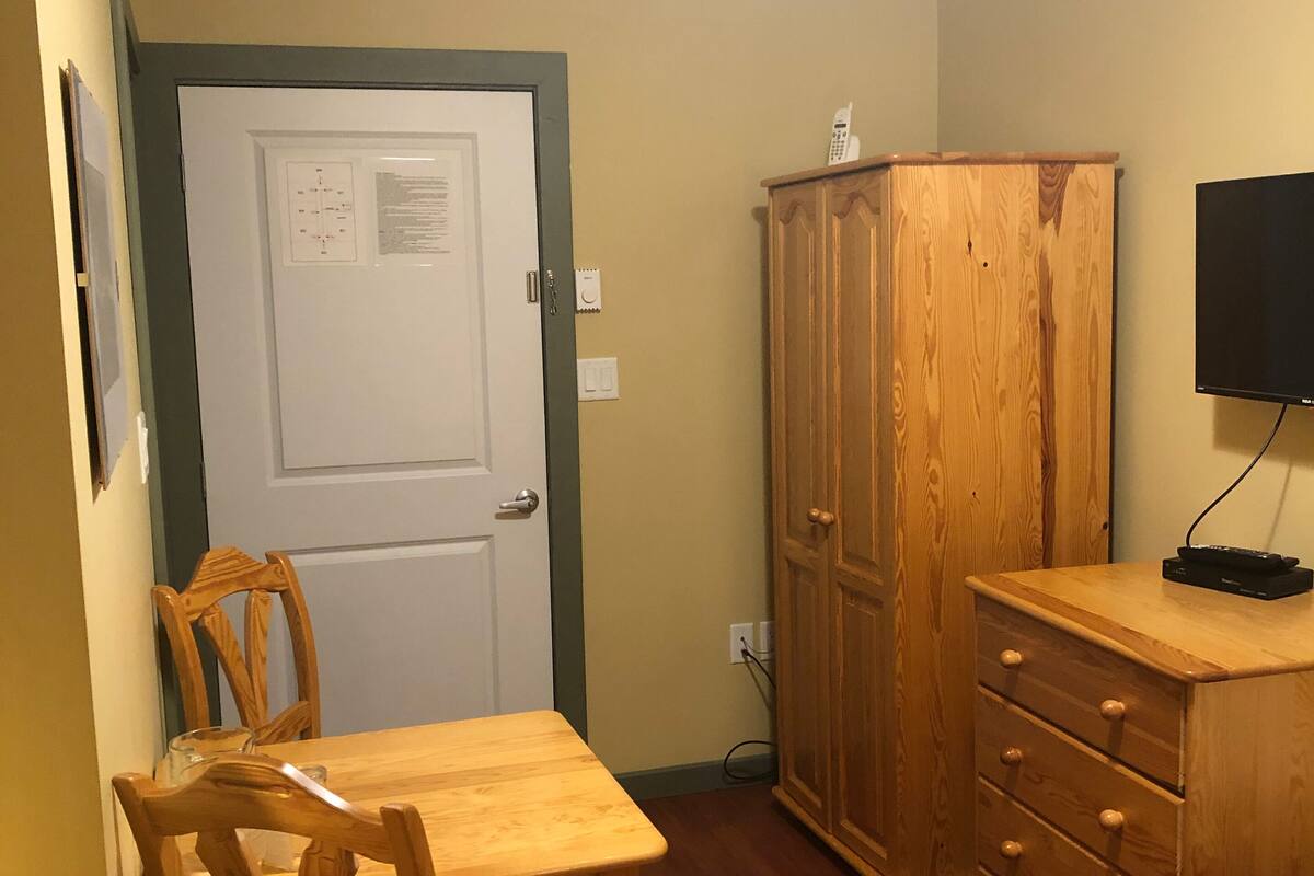 Une pièce de taille modeste, comprenant une table et des chaises en bois, un buffet en bois et un téléviseur posé sur un meuble.