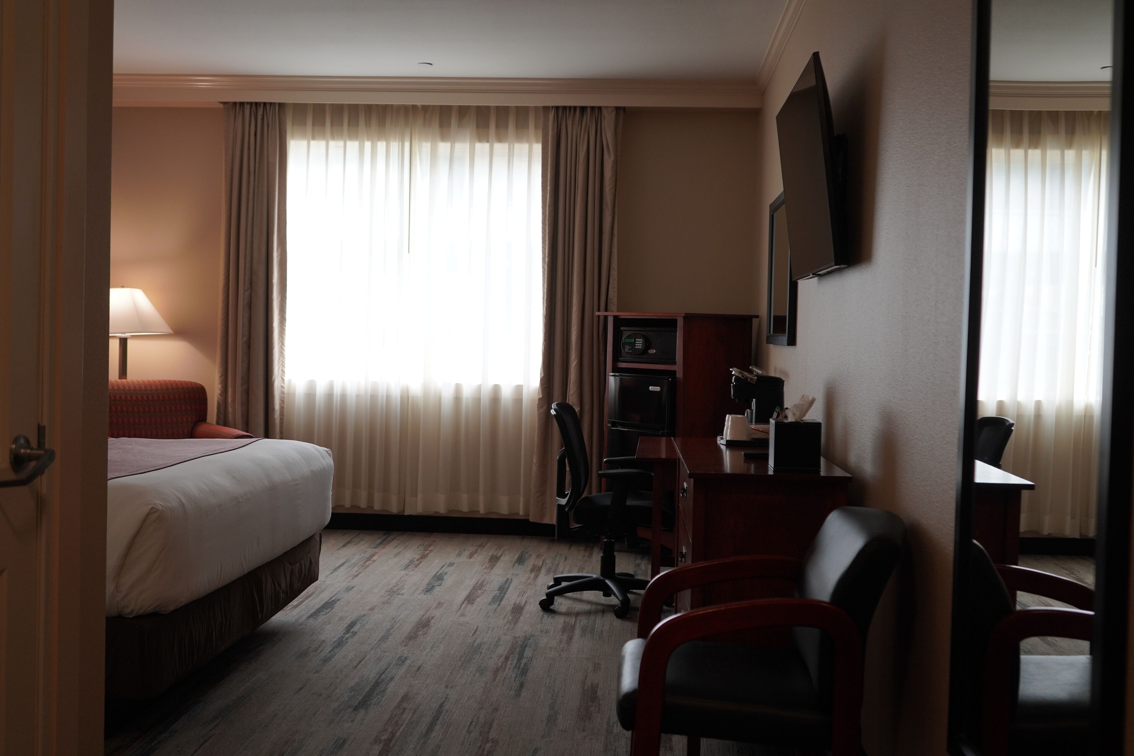 Een hotelkamer met een bed, bureau, stoel, televisie en gordijnen.
