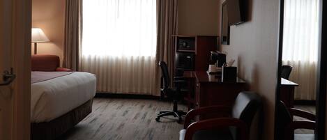 Een hotelkamer met een bed, bureau, stoel, televisie en gordijnen.