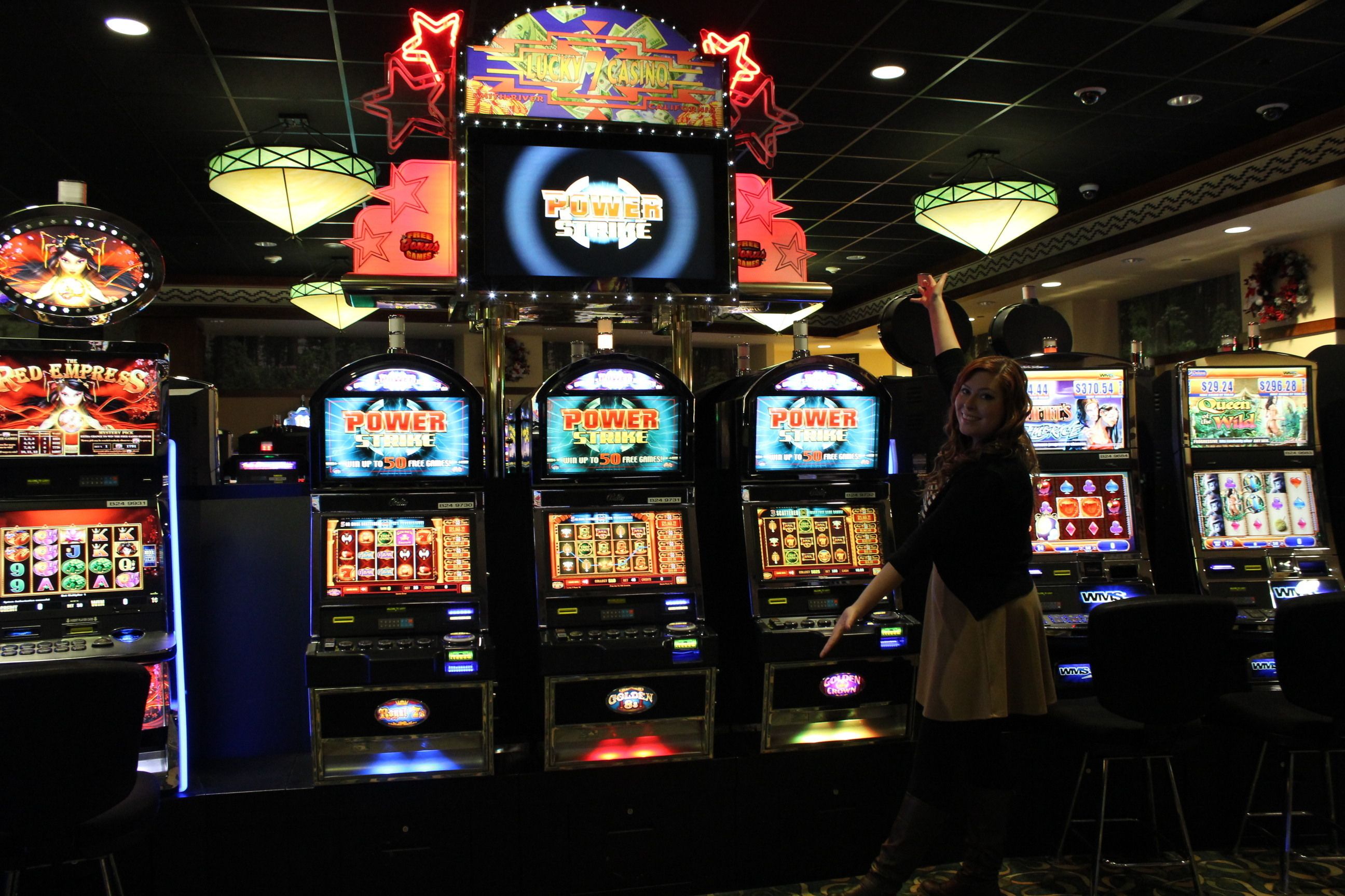 A casino with multiple slot machines, a neon sign, and a chandelier.