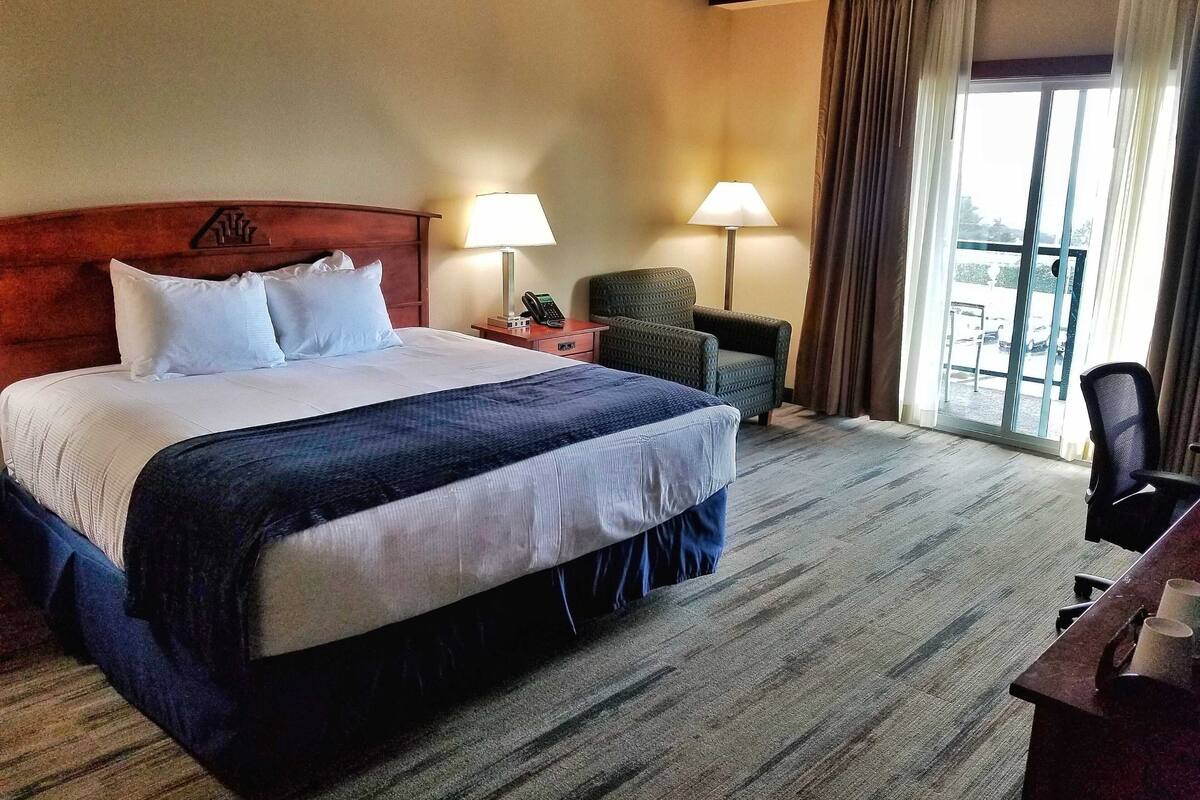 Habitación de hotel con una cama grande, dos lámparas de noche, una silla, un escritorio con su silla y vista al exterior a través de una ventana.