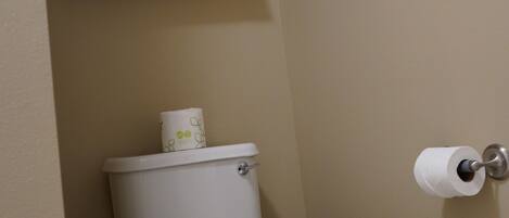 Une salle de bain avec des toilettes, un porte-serviettes avec des serviettes pliées et du papier toilette accroché au mur.