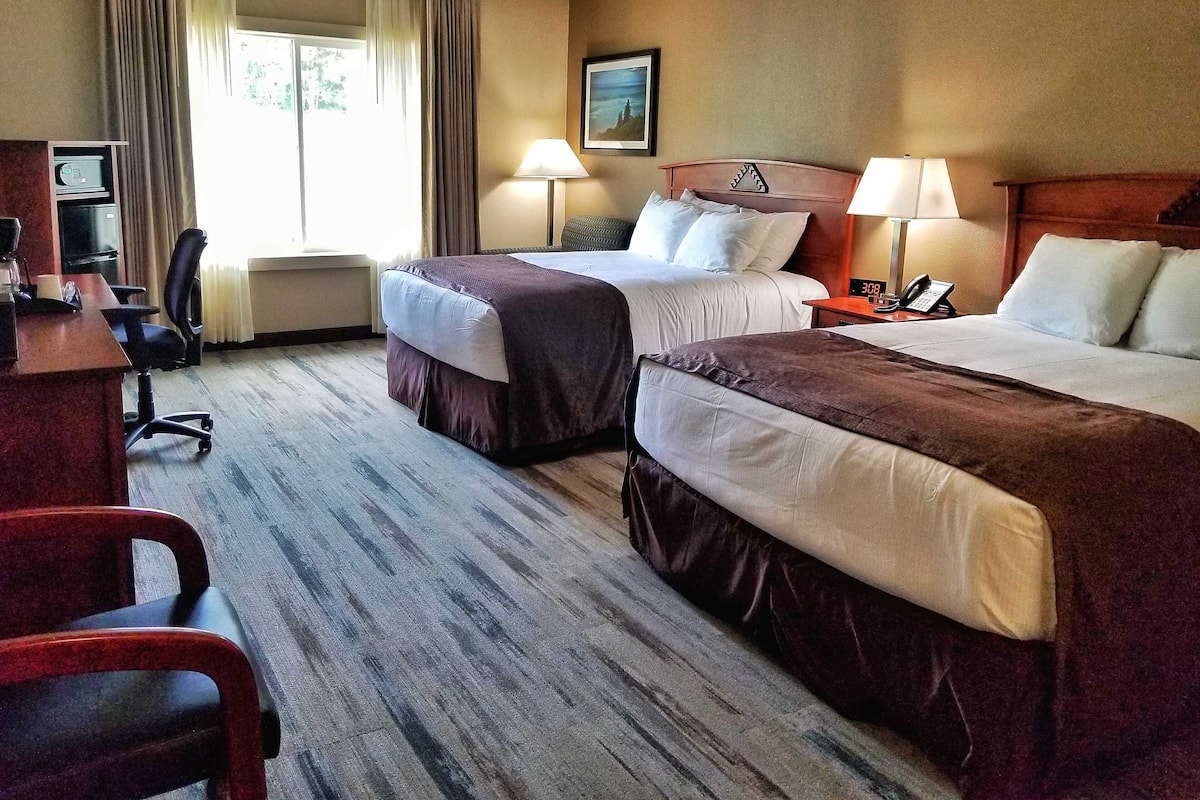 Habitación de hotel con dos camas, un escritorio, una silla, un televisor y una ventana con cortinas.