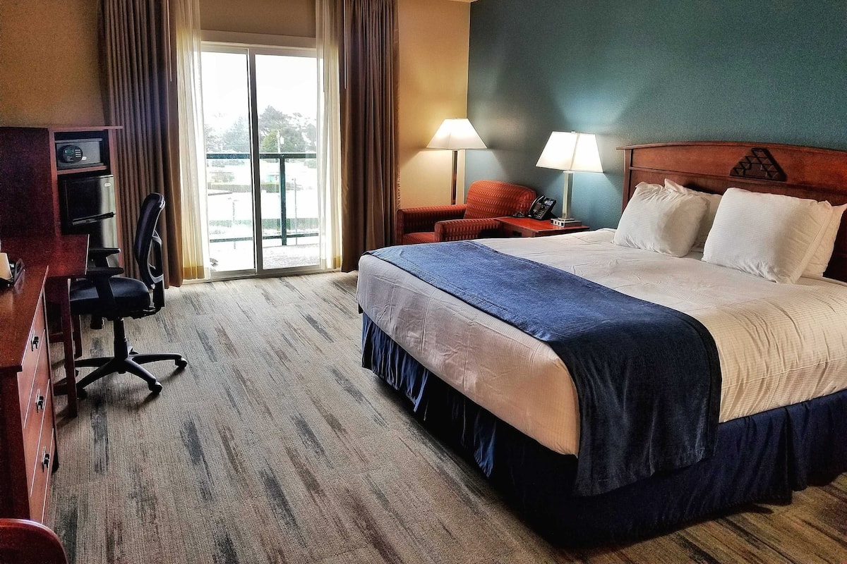 Habitación de hotel con una cama grande, un escritorio con silla, un teléfono y vista al exterior a través de una puerta corredera.