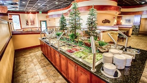 Buffet-alue, jossa on useita ruokapisteitä, puinen tiski ja koristeellisia puita.