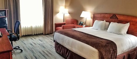 A hotel room with a large bed, two bedside lamps, a desk with a computer, and a chair.