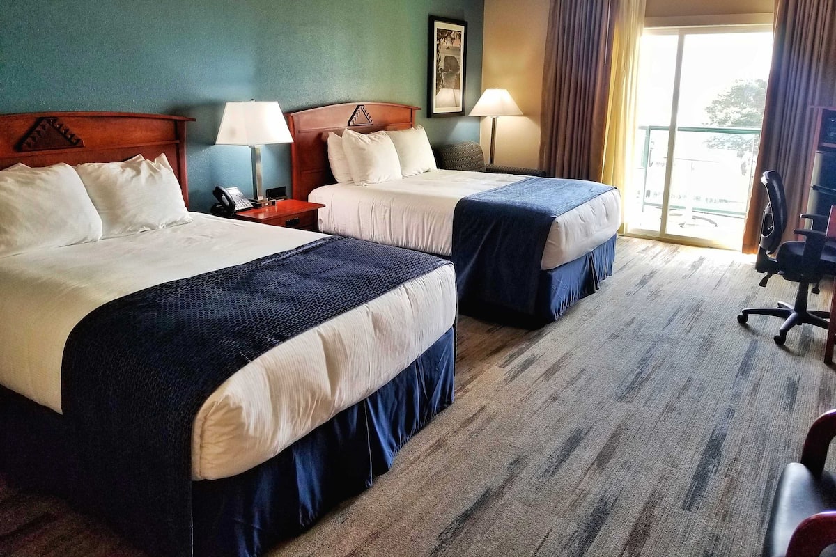 Habitación de hotel con dos camas, un escritorio, una silla y una ventana con cortinas.