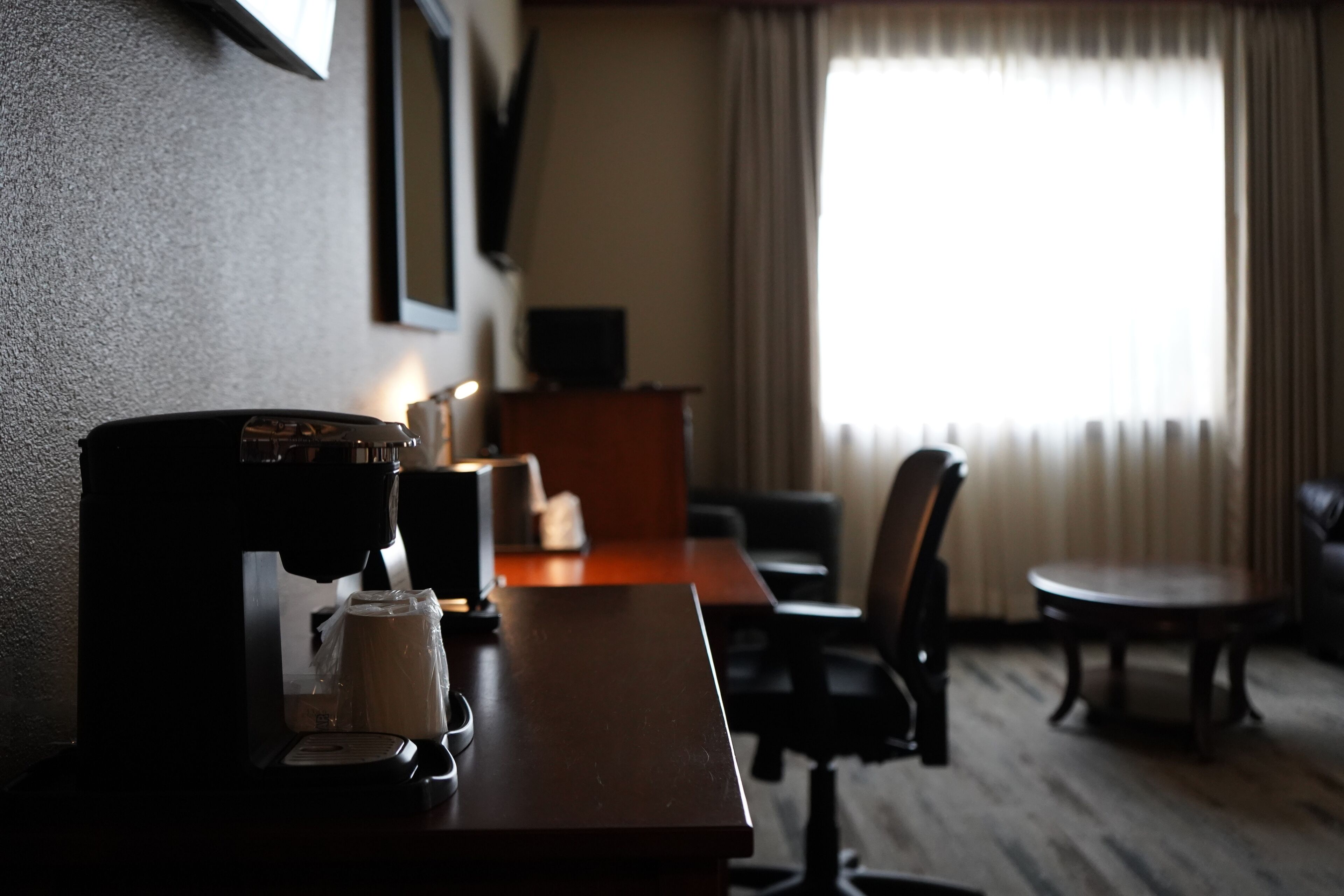 A hotel room with a coffee machine, a small table, a chair, and a sofa.