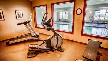 Ein Fitnessraum mit Trainingsgeräten, Blick auf einen Pool und einer Wanduhr.