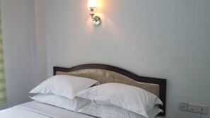 Una cama bien tendida con sábanas blancas y un cabecero de madera, una lámpara de pared y un enchufe en la pared.