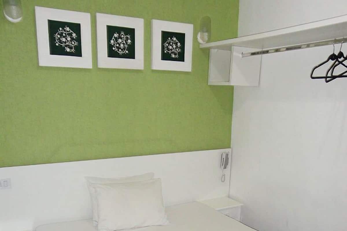 A hotel room with a green wall, a white bed, a white nightstand, and a white wardrobe.