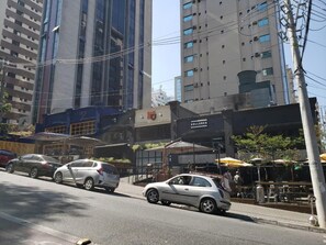 A street view with parked cars, a restaurant with outdoor seating, and tall buildings in the background. - Hotel Recanto das Perdizes (São Paulo)