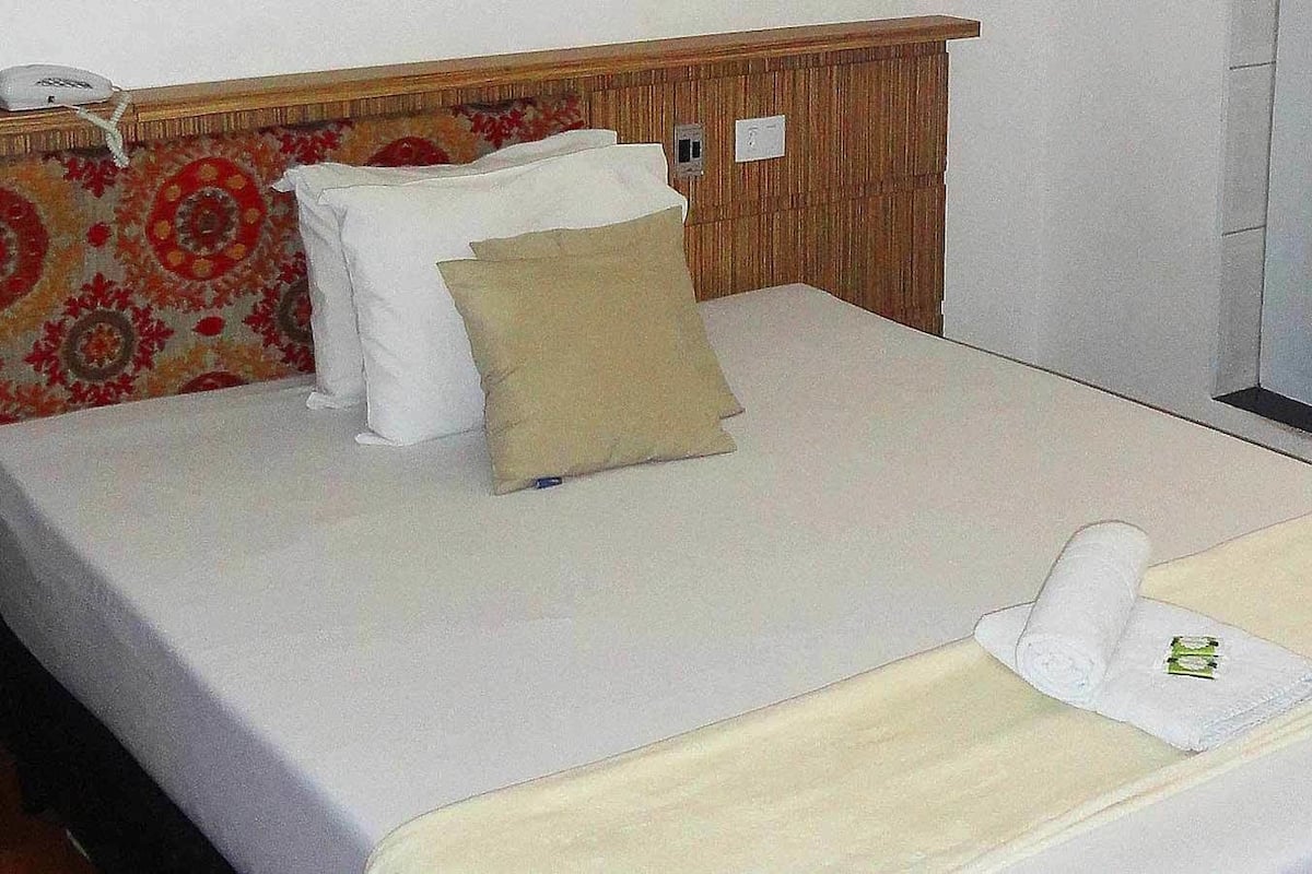 A neatly made bed with a white duvet, a beige pillow, and a white pillow.
