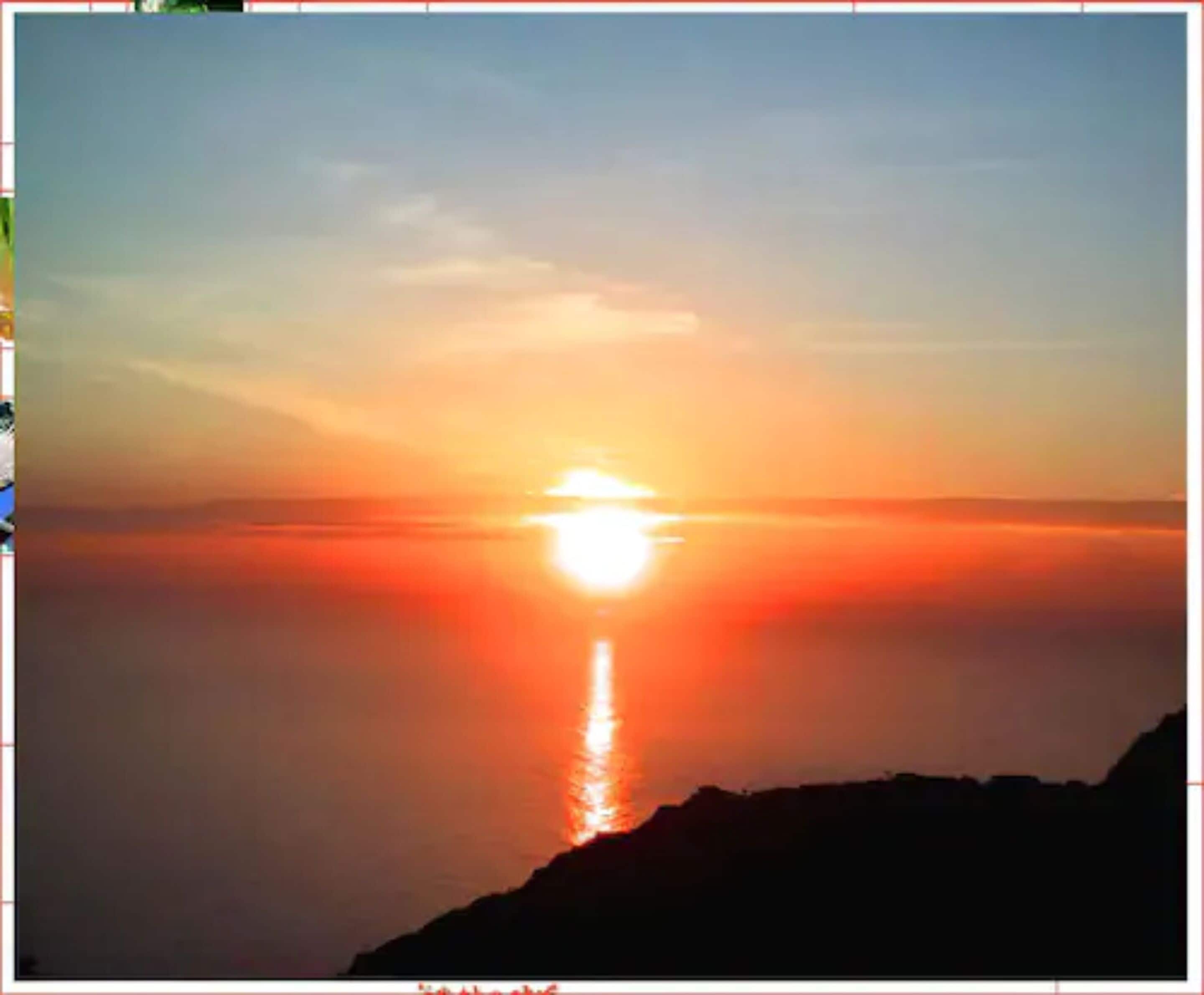 Un atardecer sobre un mar tranquilo, con la silueta de una cadena montañosa al frente.