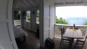 A cozy room with a wooden table and chairs, a bed, and a window overlooking greenery. - El Momo Cottages (Windward Side)