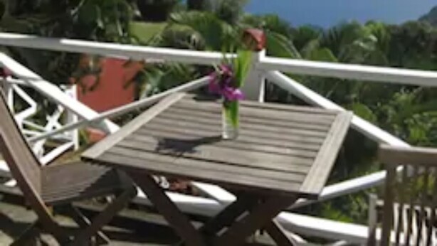 A wooden deck with lounge chairs and a table, overlooking a scenic view of the ocean and lush greenery. - El Momo Cottages (Windward Side)