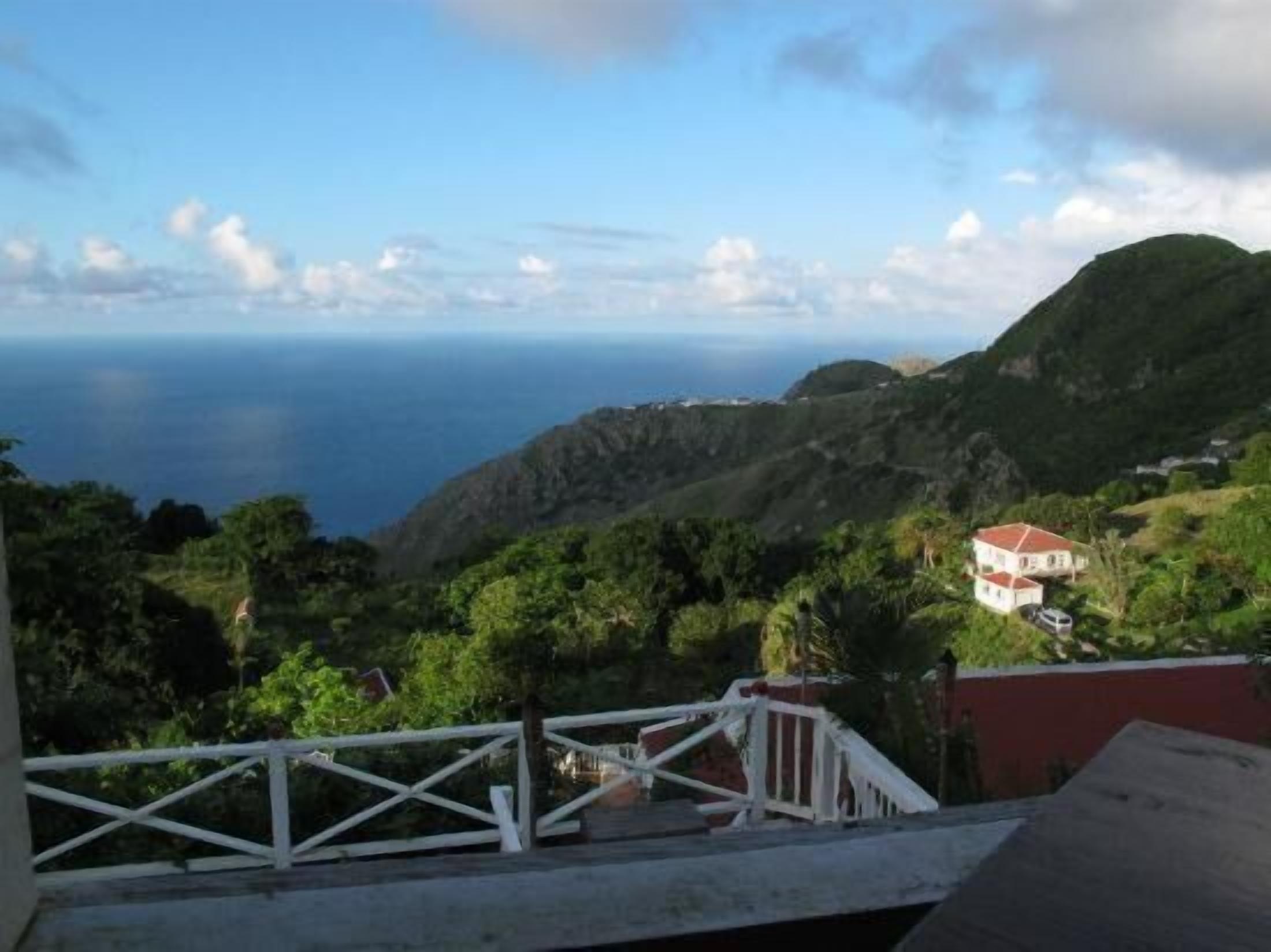 A coastal view with a house on a hillside, surrounded by greenery and overlooking the sea.