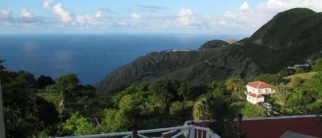 A coastal view with a house on a hillside, surrounded by greenery and overlooking the sea.