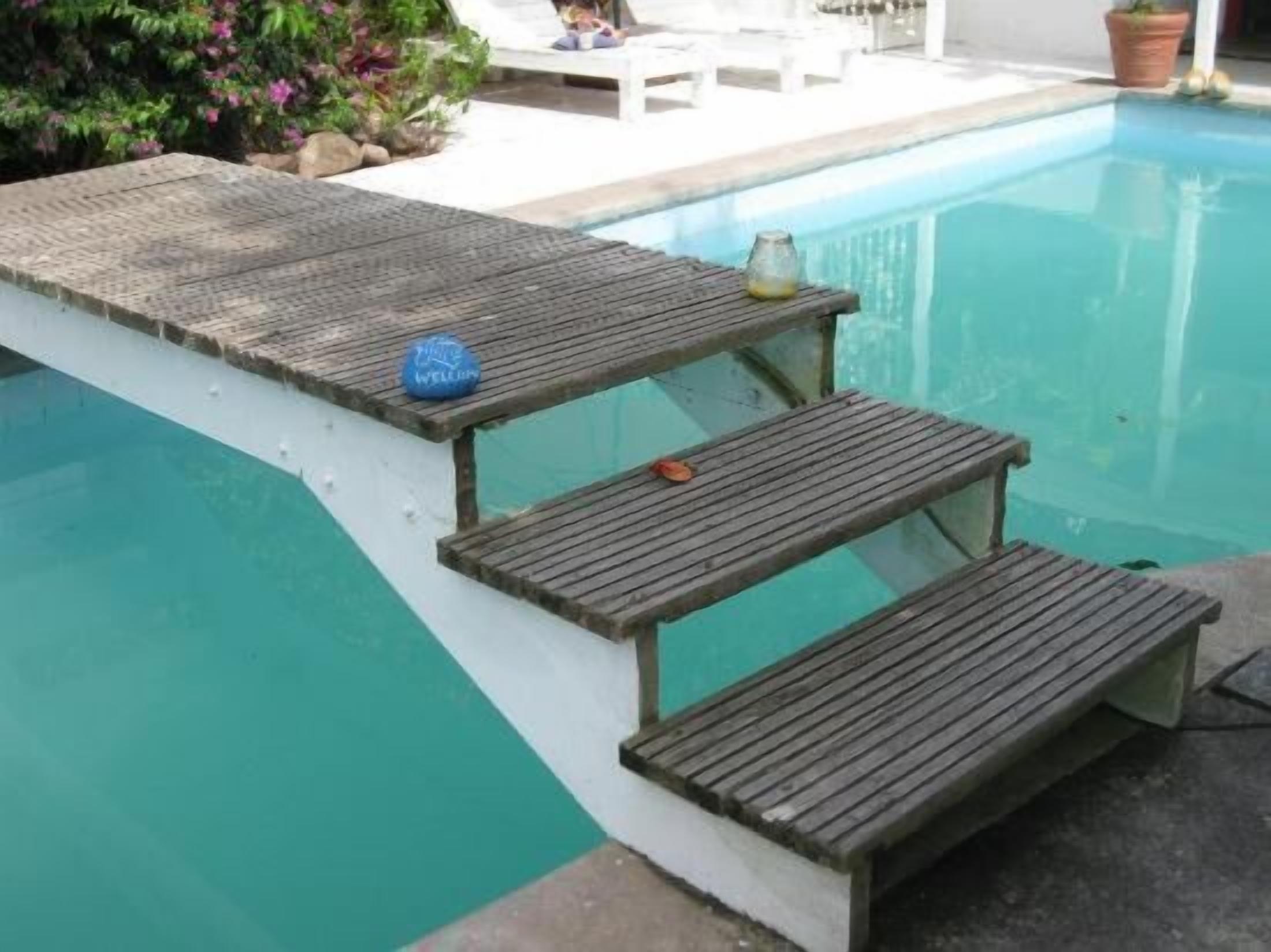 Un área junto a la piscina con cubierta de madera, una mesa pequeña con una botella y una silla de descanso.