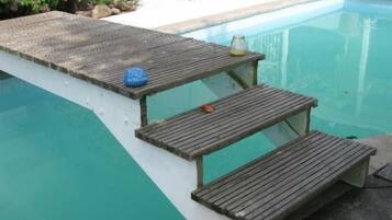 Un área junto a la piscina con cubierta de madera, una mesa pequeña con una botella y una silla de descanso.
