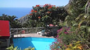 A pool surrounded by lush greenery and a view of the ocean. - El Momo Cottages (Windward Side)