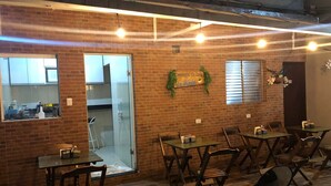 Un restaurante con paredes de ladrillo, mesas y sillas de madera. Hay una partición de vidrio que separa el área de comedor de la cocina.