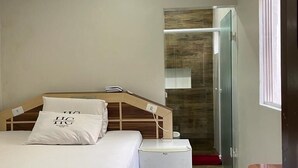 Un dormitorio con cama, mesita de noche y baño pequeño con ducha.