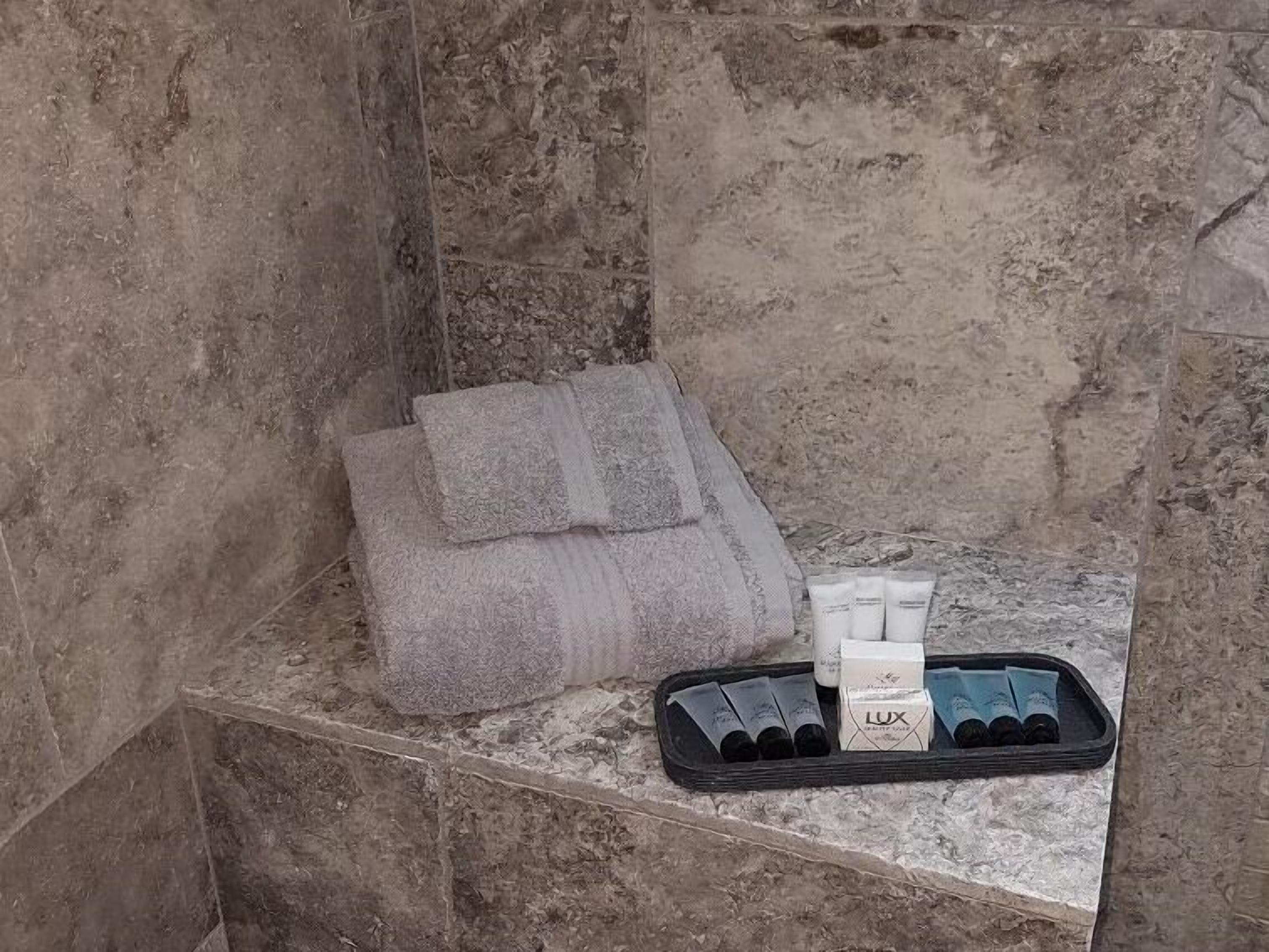 Une salle de bain avec un mur en marbre, une serviette et des articles de toilette disposés sur un plateau.