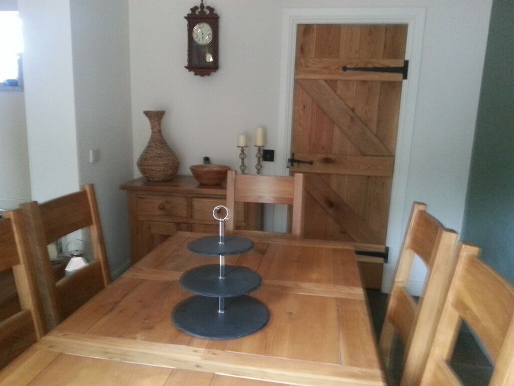 Comedor con una mesa de madera, sillas, un florero, un reloj y una puerta de madera.