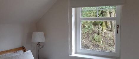 Un dormitorio con cama, mesita de noche, lámpara y ventana con vistas a árboles.
