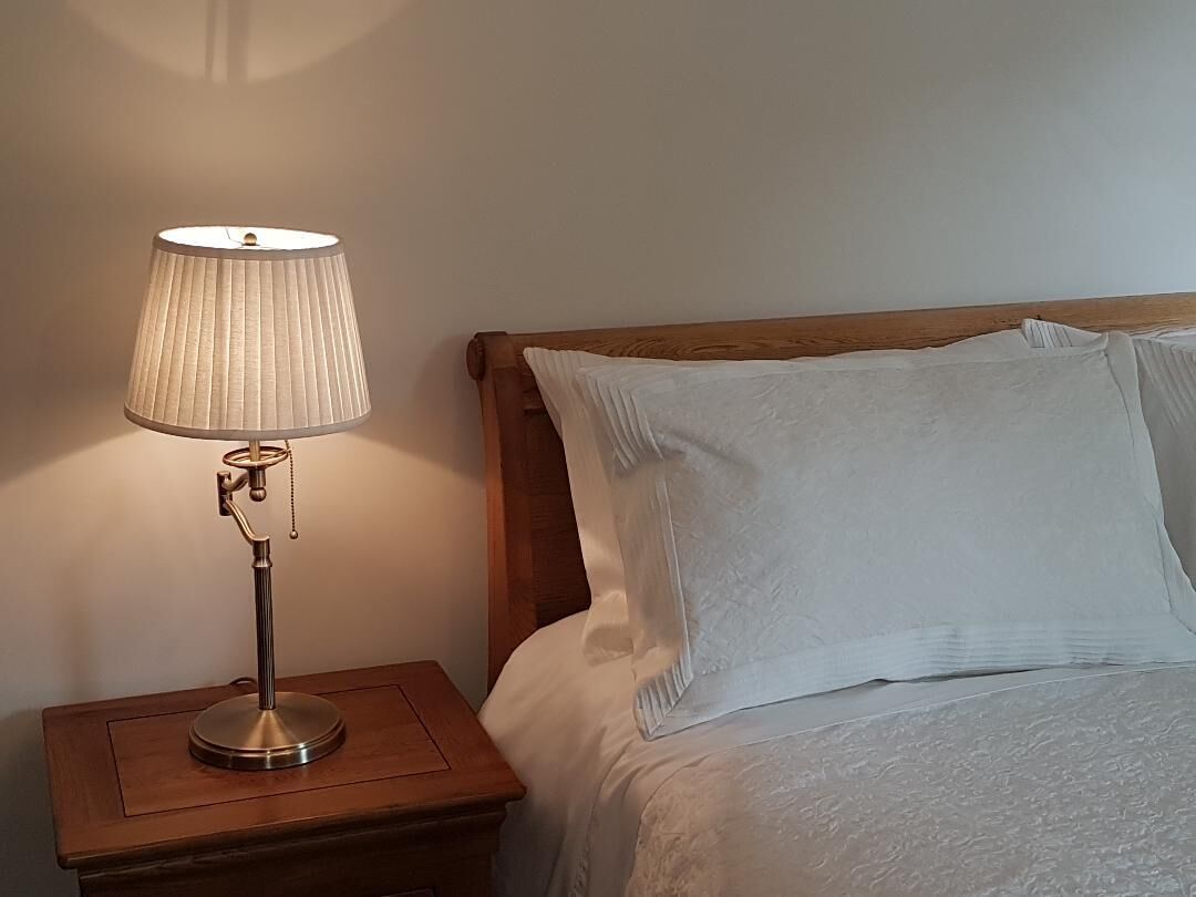 Ein Bett mit weißer Bettwäsche und einem hölzernen Kopfteil, ein Nachttisch mit Lampe und ein weiterer Holz-Nachttisch.