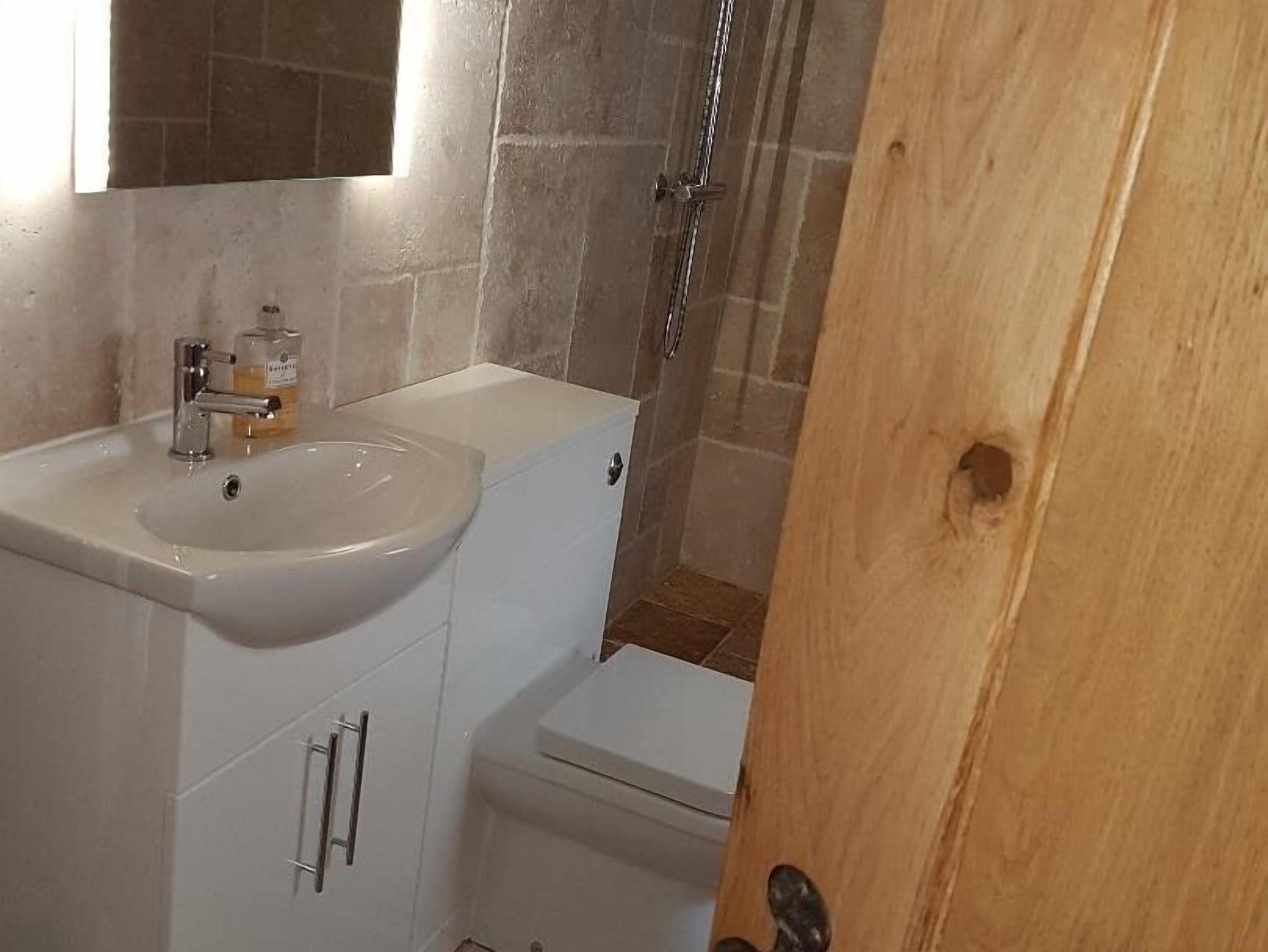 Un baño con lavamanos blanco, espejo y zona de ducha.