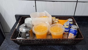 A kitchen counter with a wicker basket containing a bottle, two plastic cups with orange liquid, a metal container, and a jar of honey. - Hotel Diamantina Av. Brigadeiro Bela Vista SP (São Paulo)