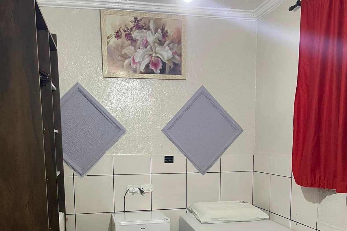 A small, clean room with a bed, a small white heater, and a ceiling fan.