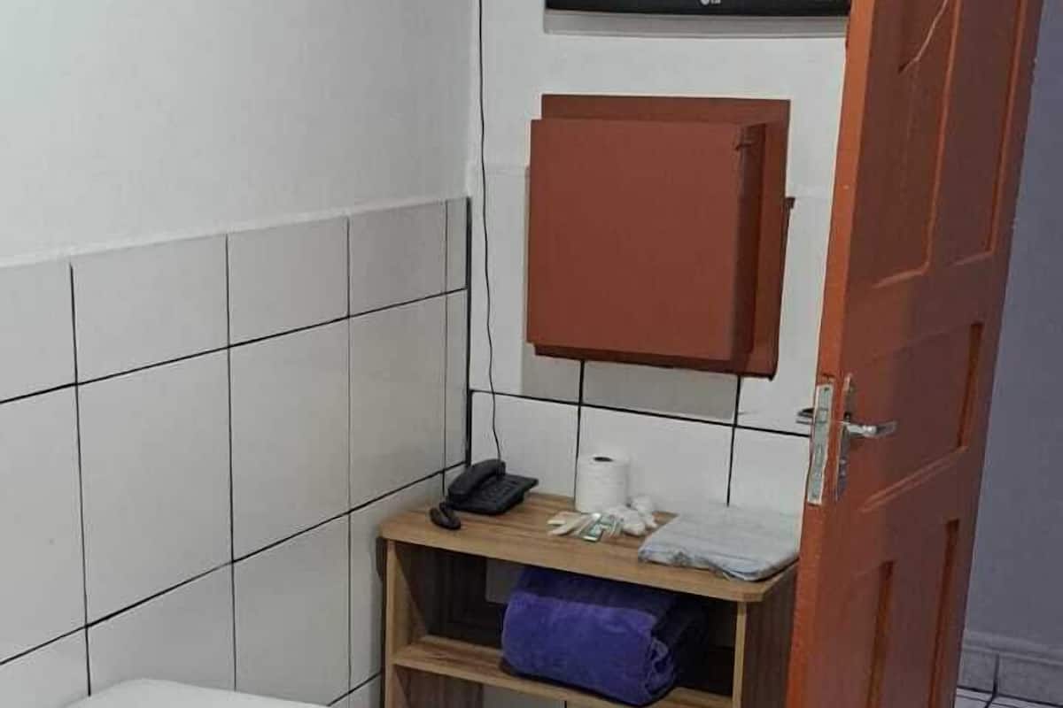 A small, clean room with a bed, a wooden nightstand, a TV mounted on the wall, and a door.