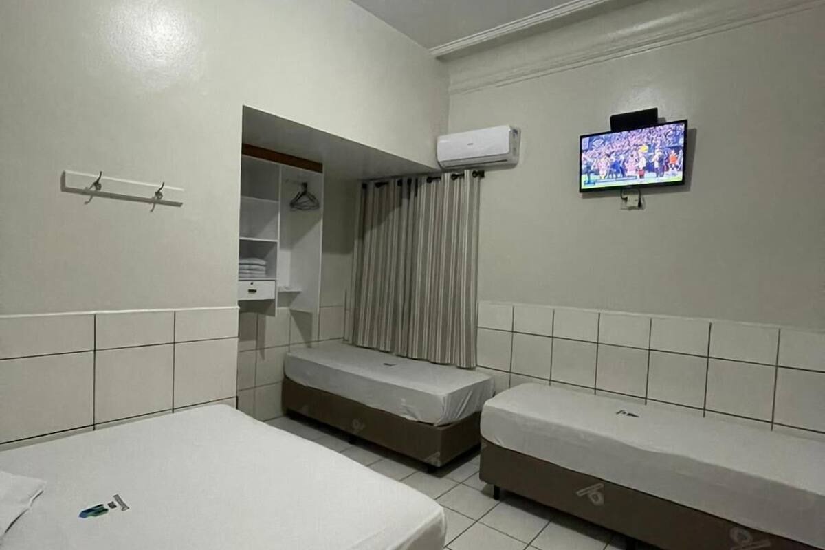 A hotel room with two single beds, a TV mounted on the wall, an air conditioning unit, and a small seating area with a curtain.