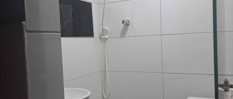 A small, modern bathroom with white tiles, a black countertop, a white sink, and a toilet.