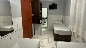 A small, clean room with two single beds, a wooden wardrobe, a mirror, a television, and a shower curtain. - Hotel Diamantina Av. Brigadeiro Bela Vista SP (São Paulo)
