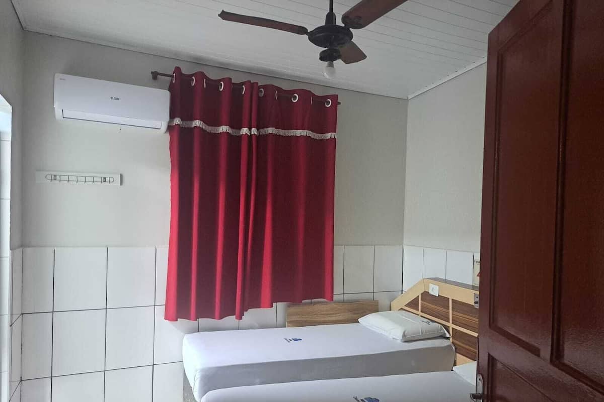 A room with two beds, a ceiling fan, and a red curtain.