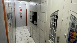 A hallway with tiled floors, a fire extinguisher, a door with a window, and a wall-mounted shelf. - Hotel Diamantina Av. Brigadeiro Bela Vista SP (São Paulo)