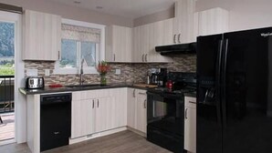 A modern kitchen with white cabinets, a black refrigerator, and a stone backsplash. - Klippers Guest Suites (Keremeos)