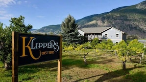A sign for 'Klippers Guest Suites' with a vineyard and mountains in the background. - Klippers Guest Suites (Keremeos)