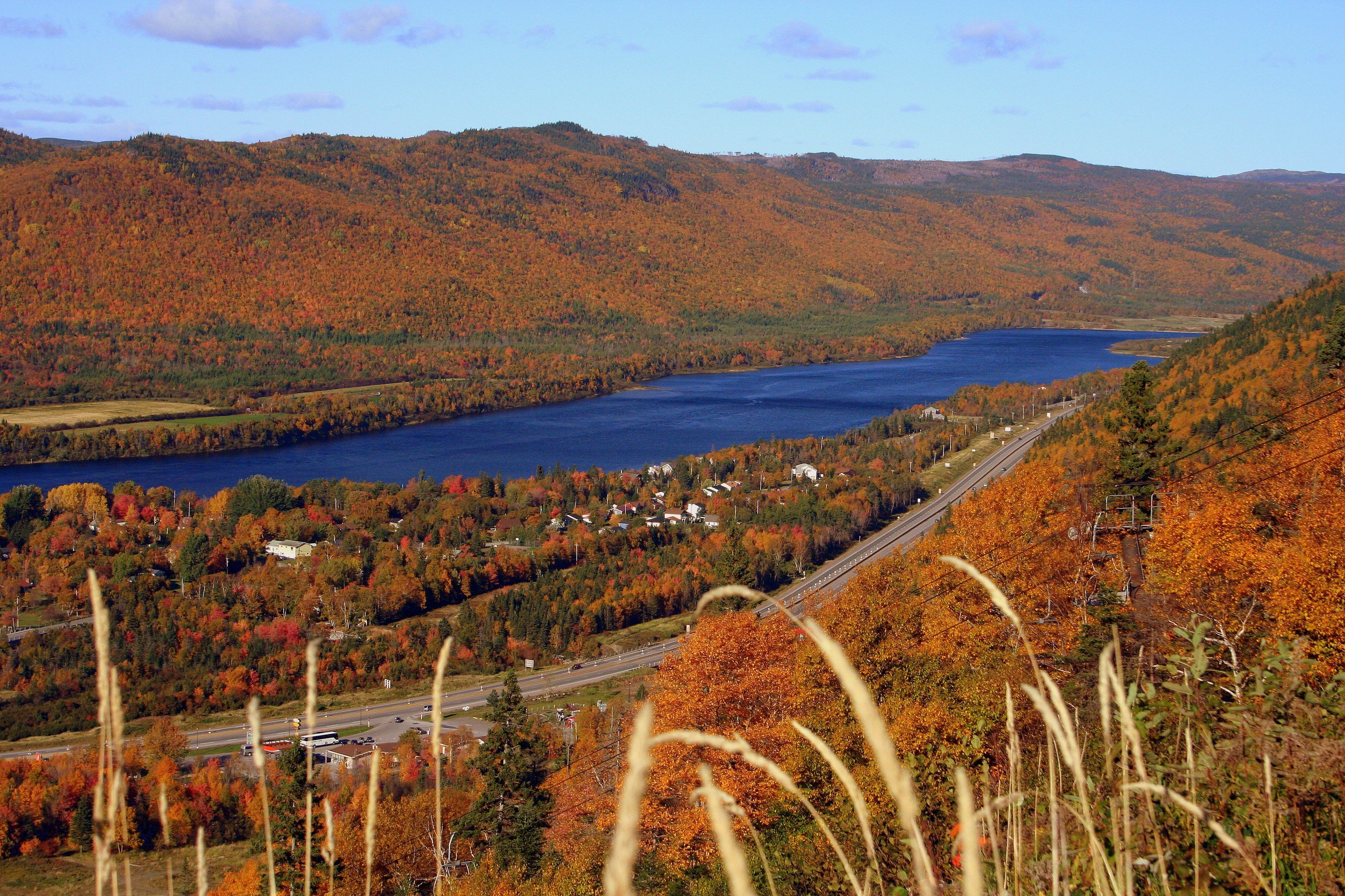 Un paysage magnifique : un lac entouré de collines aux couleurs automnales, une autoroute et un petit village.