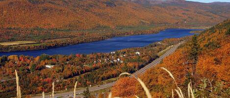 Un paysage magnifique : un lac entouré de collines aux couleurs automnales, une autoroute et un petit village.