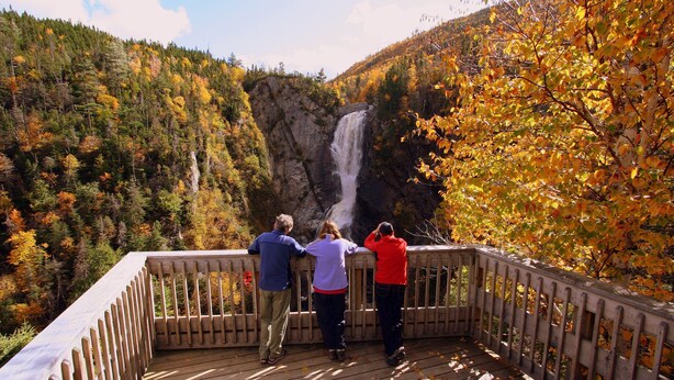 Una terraza de madera con vistas a una cascada y un paisaje boscoso de fondo.